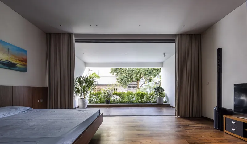 Bedroom opening through floor-to-ceiling glass to terrace with potted trees