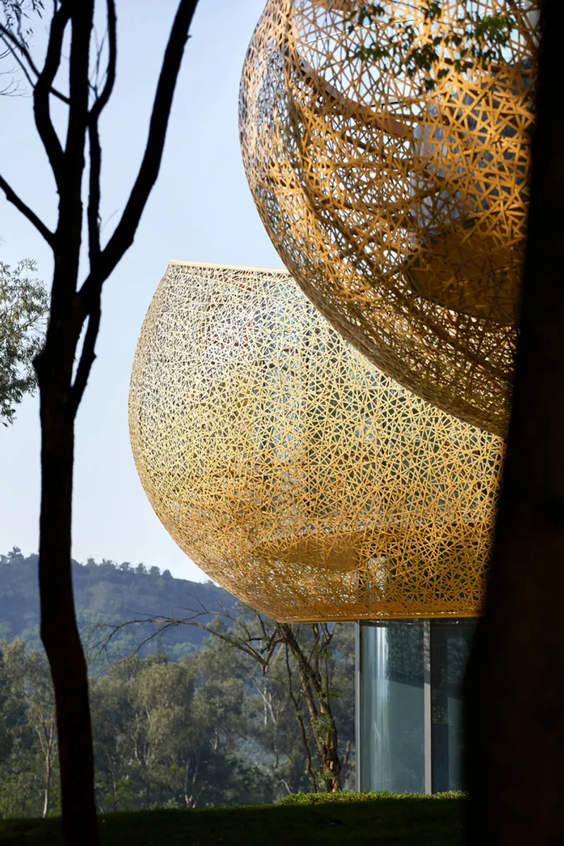 Perforated golden metal volumes stacked near a bare tree with distant hills beyond