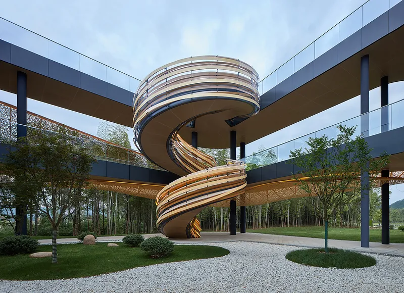 Helical staircase with layered metal ribbons beneath elevated walkways and planted landscape