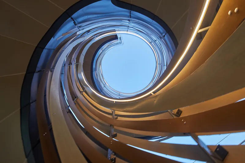Upward view through a spiral atrium with layered curved balconies and integrated linear lighting