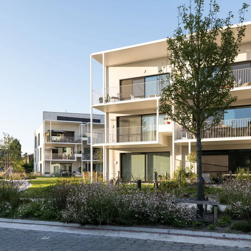 Street view of the residential block with stacked balconies and planted garden beds in afternoon light
