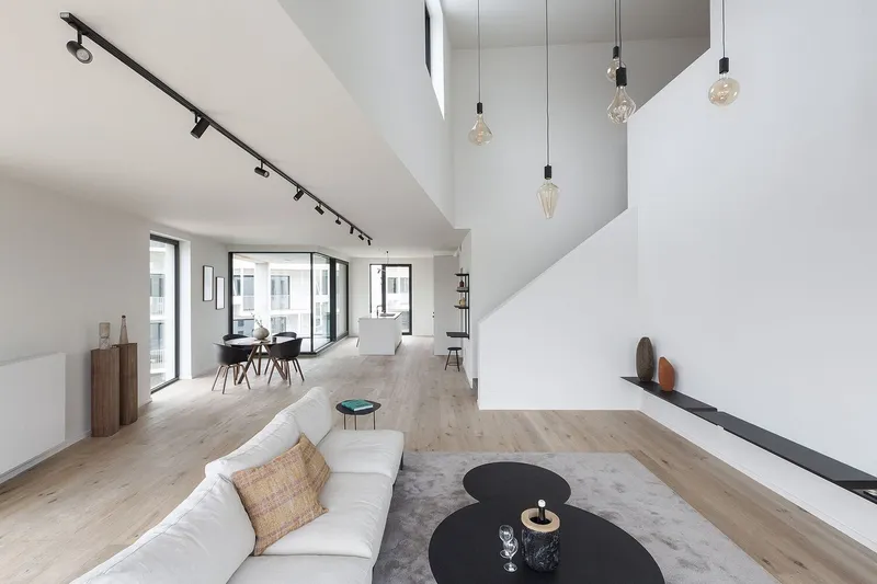 Double-height living room with pale timber flooring and track lighting beneath a skylight void