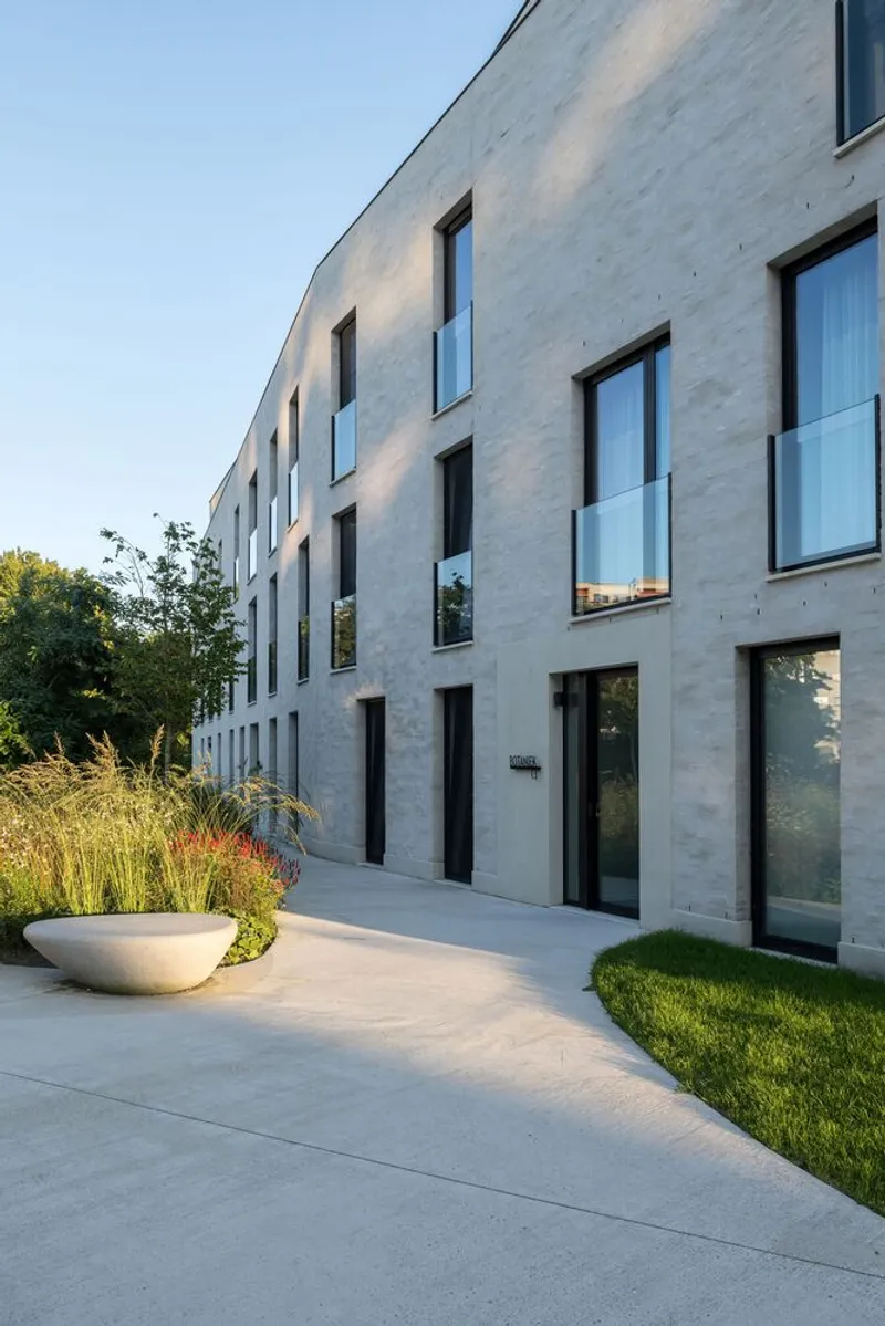 Concrete facade with punched windows and ground-level terrace beside ornamental grasses at dusk