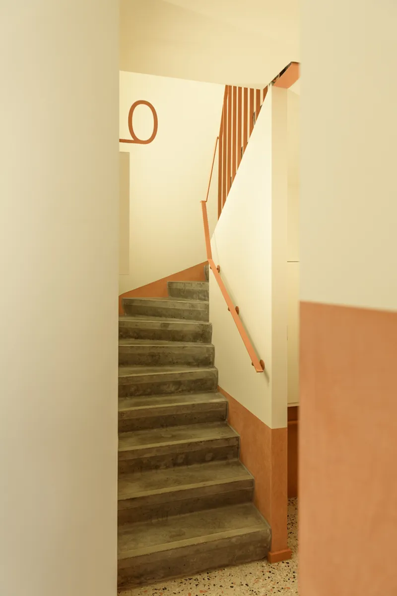 Concrete staircase with terracotta base and timber handrail in a cream-painted stairwell with warm afternoon light