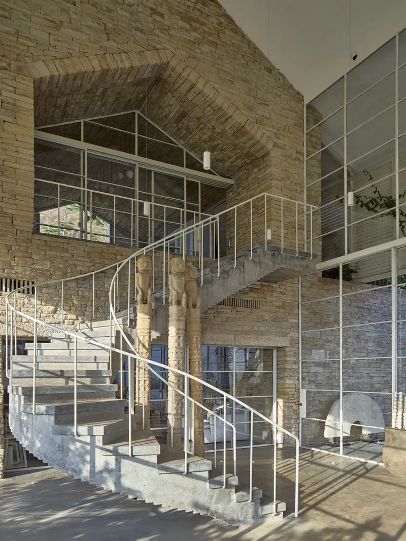Curved concrete staircase with tubular steel railings ascending beneath a barrel-vaulted brick ceiling in afternoon light