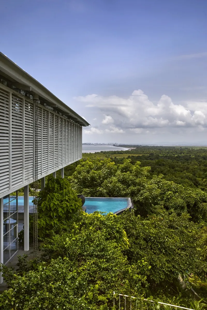 Elevated infinity pool cantilevered above dense tropical forest canopy with louvered facade under cumulus clouds