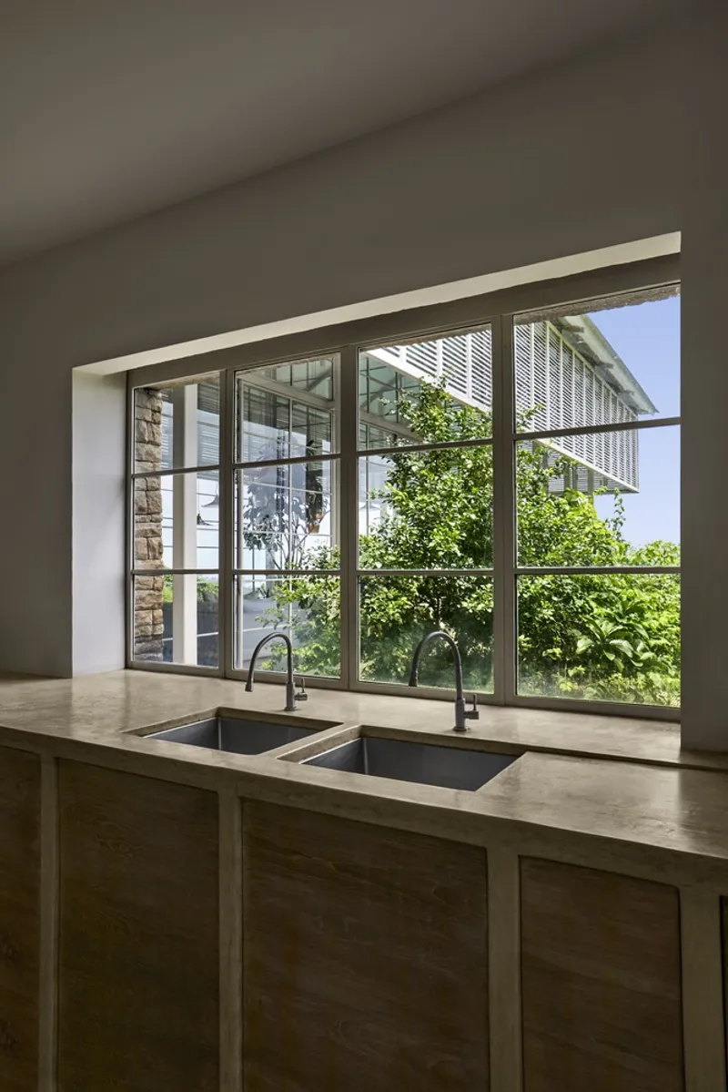 Kitchen island with integrated sink facing full-height glazing that opens to planted courtyard with louvers beyond