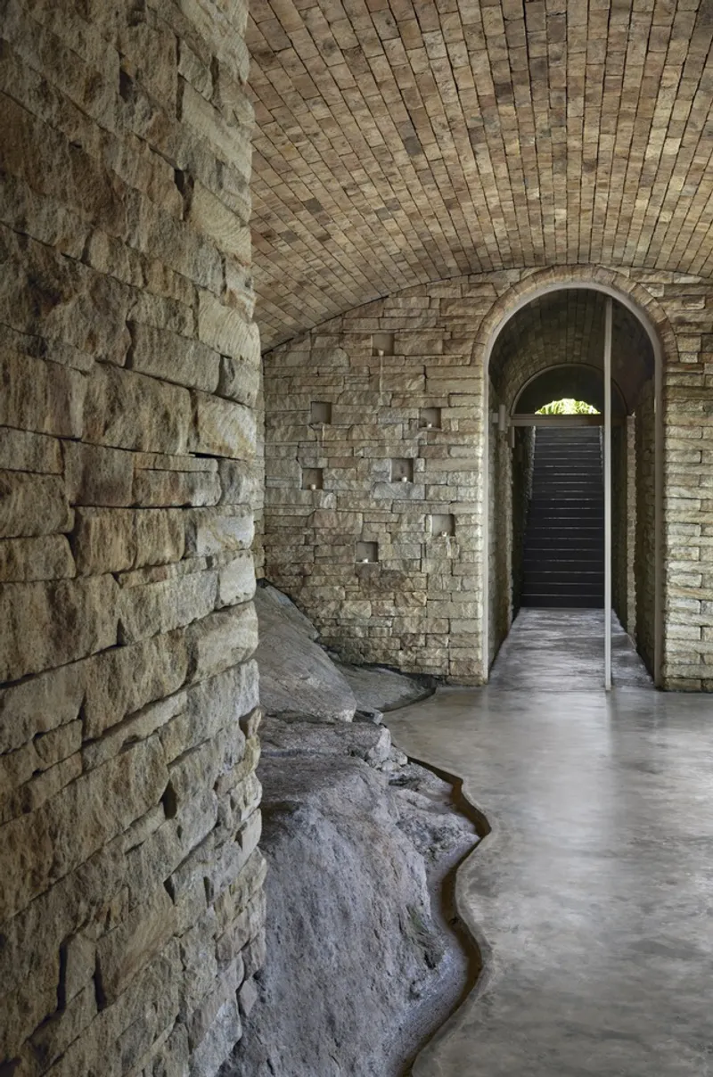 Interior passageway with curved stone bench and vaulted brick ceiling framing distant archway to exterior