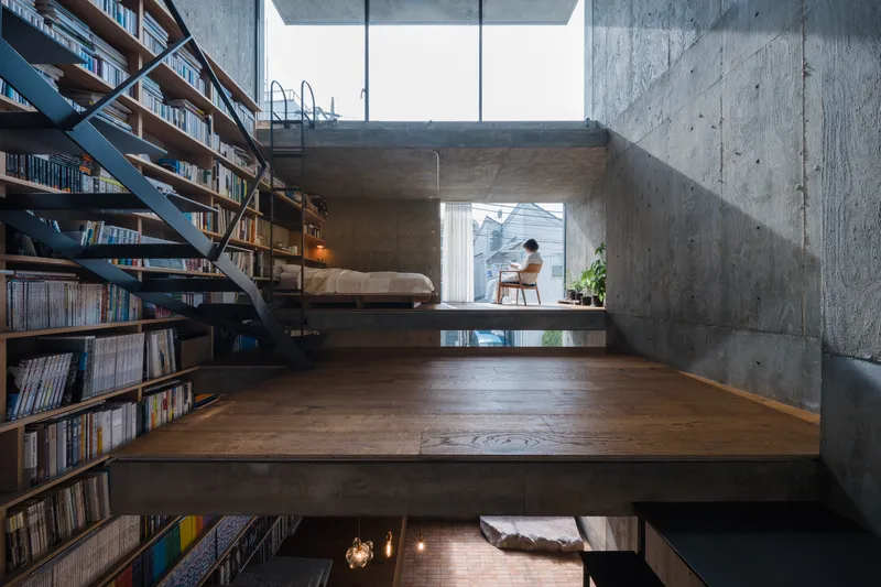 Split-level interior with timber floor platforms, board-formed concrete walls, and a figure seated in daylight beyond