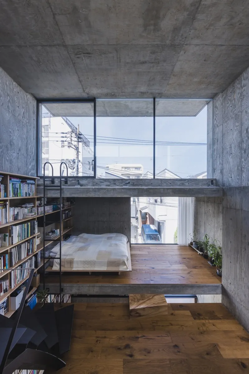 Concrete-framed bedroom level with large window overlooking neighboring rooftops and power lines in hazy light