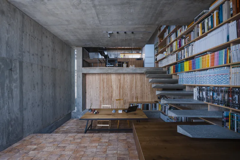 Double-height library space with cantilevered concrete stair treads, timber dining table, and terracotta tile floor inset