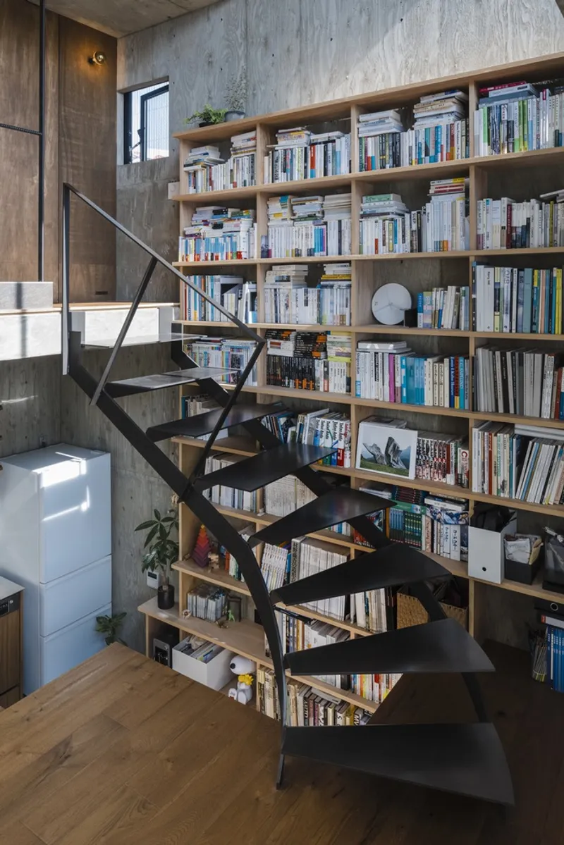 Blackened steel staircase cutting diagonally across a tall bookshelf wall with morning light from the window above
