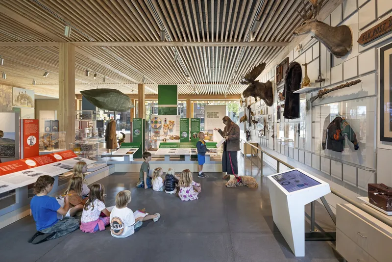 Museum hall with slatted wood ceiling and children seated on the floor during a group activity