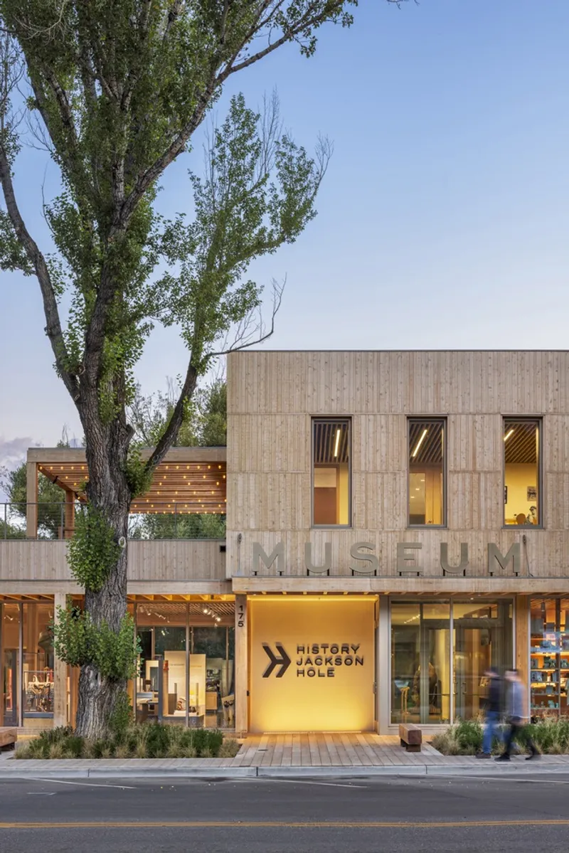 Facade at dusk showing vertical timber cladding with raised lettering and illuminated glazed entrance below