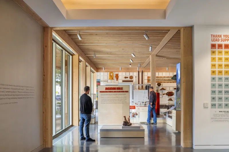 Interior gallery with wood slat ceiling and exhibition displays between visitors viewing the artifacts and wall panels