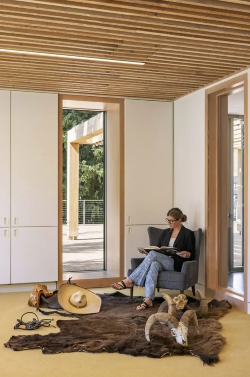 Reading nook with person seated on armchair beside window opening to the exterior timber colonnade