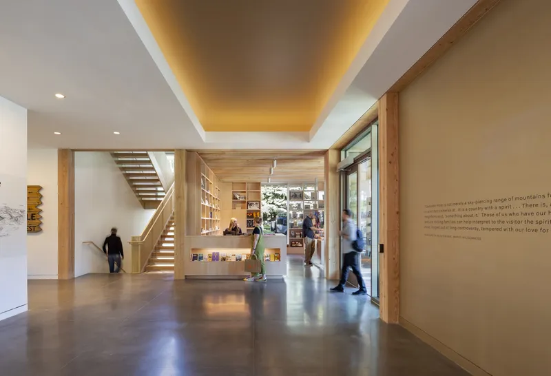 Entry hall with concrete floor showing timber staircase, backlit yellow ceiling coffer and visitors in motion