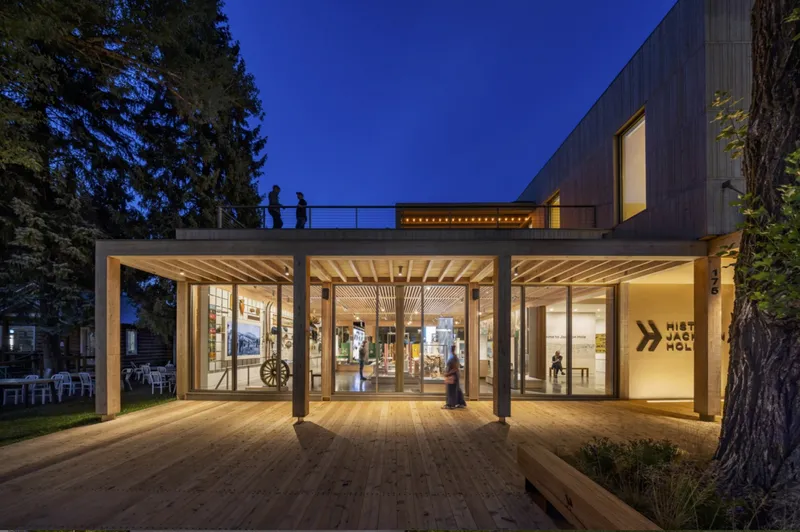 Exterior entry with timber deck, exposed beam ceiling and rooftop terrace silhouetted against dusk sky
