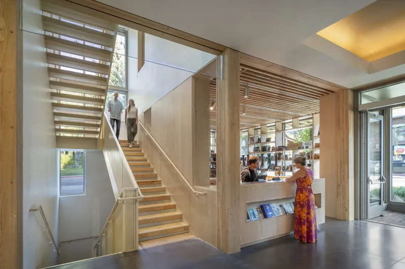 View through timber doorway to open-tread staircase as visitors descend toward the glass entrance