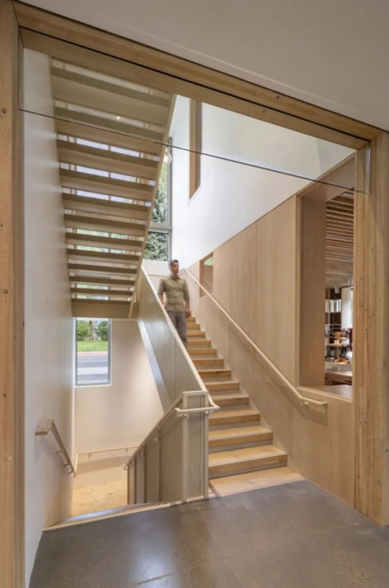 Framed view of timber staircase with glass guardrail and figure descending in afternoon light