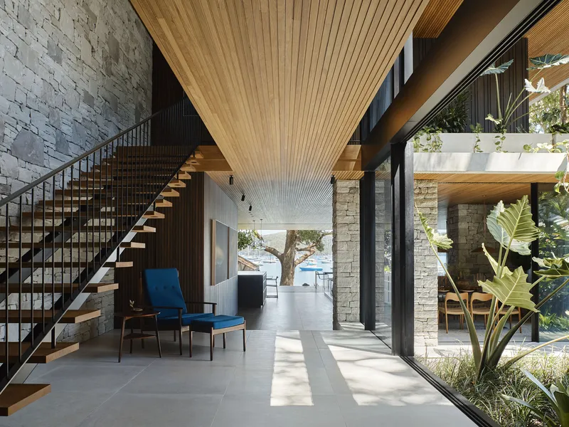 Double-height living space with timber slatted ceiling, open timber staircase, and planted courtyard visible through floor-to-ceiling glazing