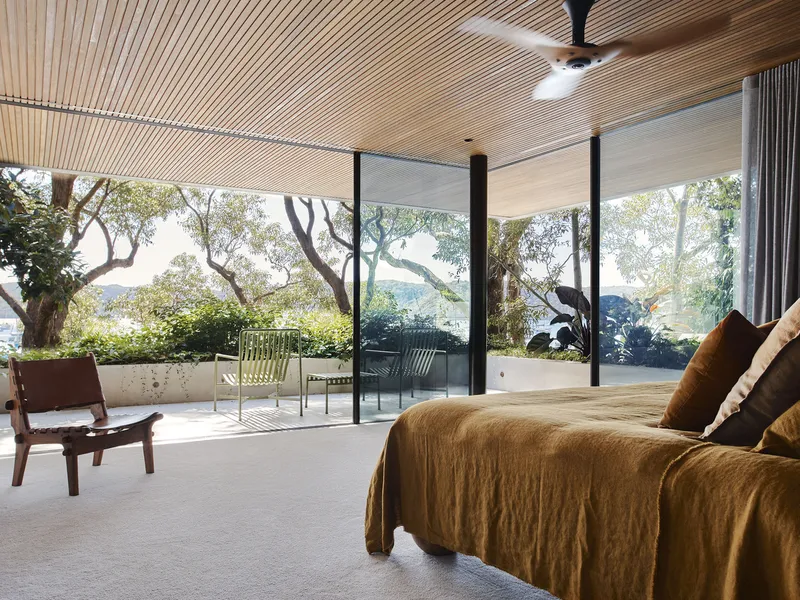 Bedroom with timber ceiling and glass doors opening to covered terrace overlooking established trees and hillside