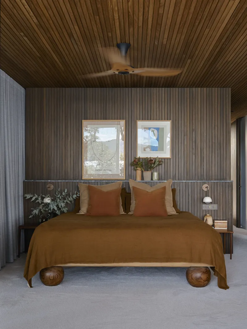 Bedroom with vertical timber cladding and slat ceiling under a spinning ceiling fan