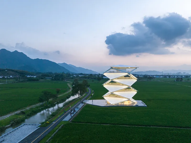 Aerial view of the zigzag stacked tower rising above green rice paddies at dusk with distant mountains