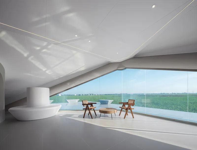 Interior space with curved ceiling, linear lighting and full-height glass overlooking the surrounding farmland