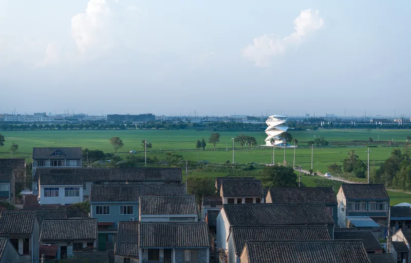 Distant view of the white tower emerging above traditional village rooftops in the flat agricultural landscape