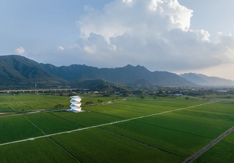 Drone perspective of the stepped white tower standing alone in the grid of green rice fields