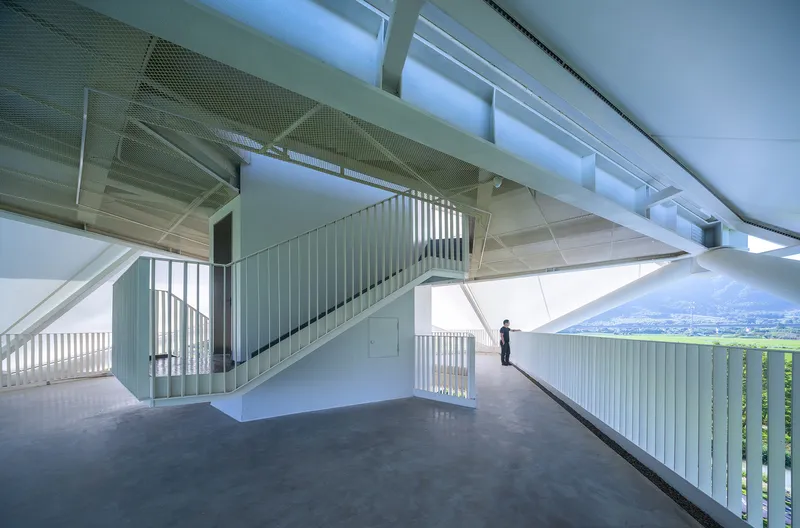 Interior staircase with white vertical slat railings and perforated metal ceiling panels admitting daylight