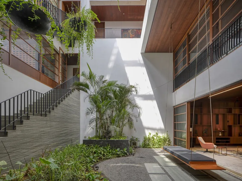 Interior courtyard with timber staircases, planted palm beds and white walls in dappled afternoon sunlight