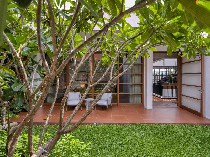 Red tile terrace with sliding screen doors opening to lawn and frangipani tree canopy