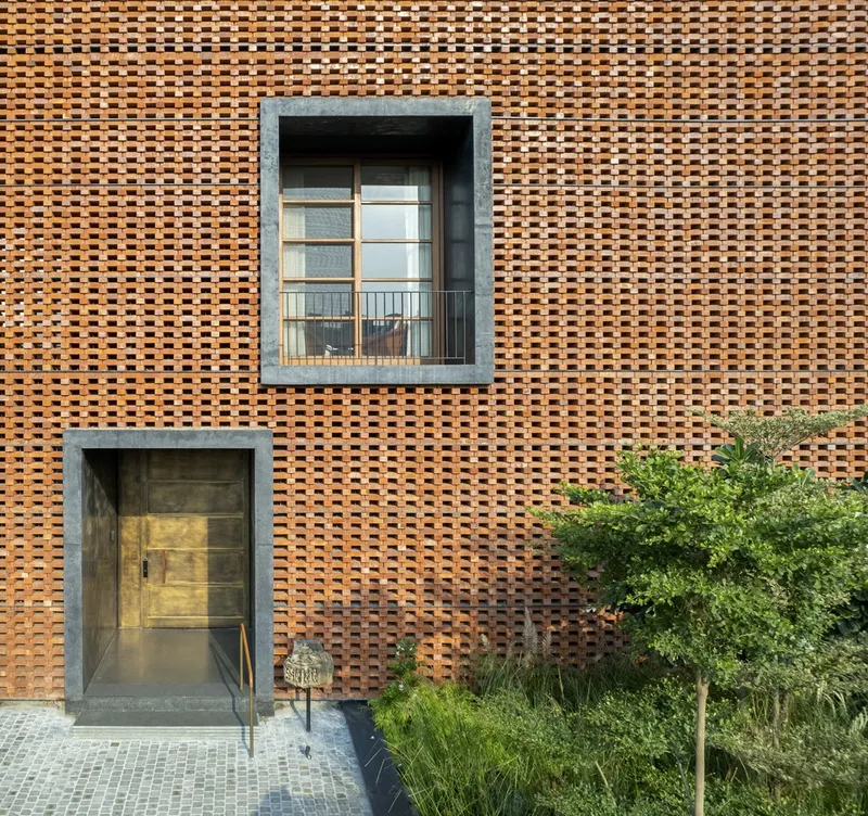 Basketweave brick facade with concrete-framed window and doorway opening beside planted shrubs and trees