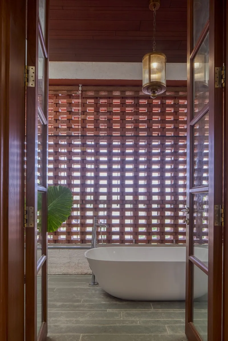 View through open timber doorway to bathroom with freestanding tub and woven brick screen wall