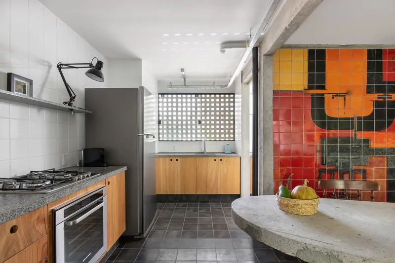 Kitchen with exposed concrete beam, timber cabinetry, and a red and orange glazed tile accent wall