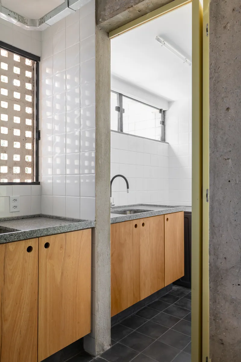 Bathroom threshold framed by exposed concrete columns with timber vanity and perforated block window