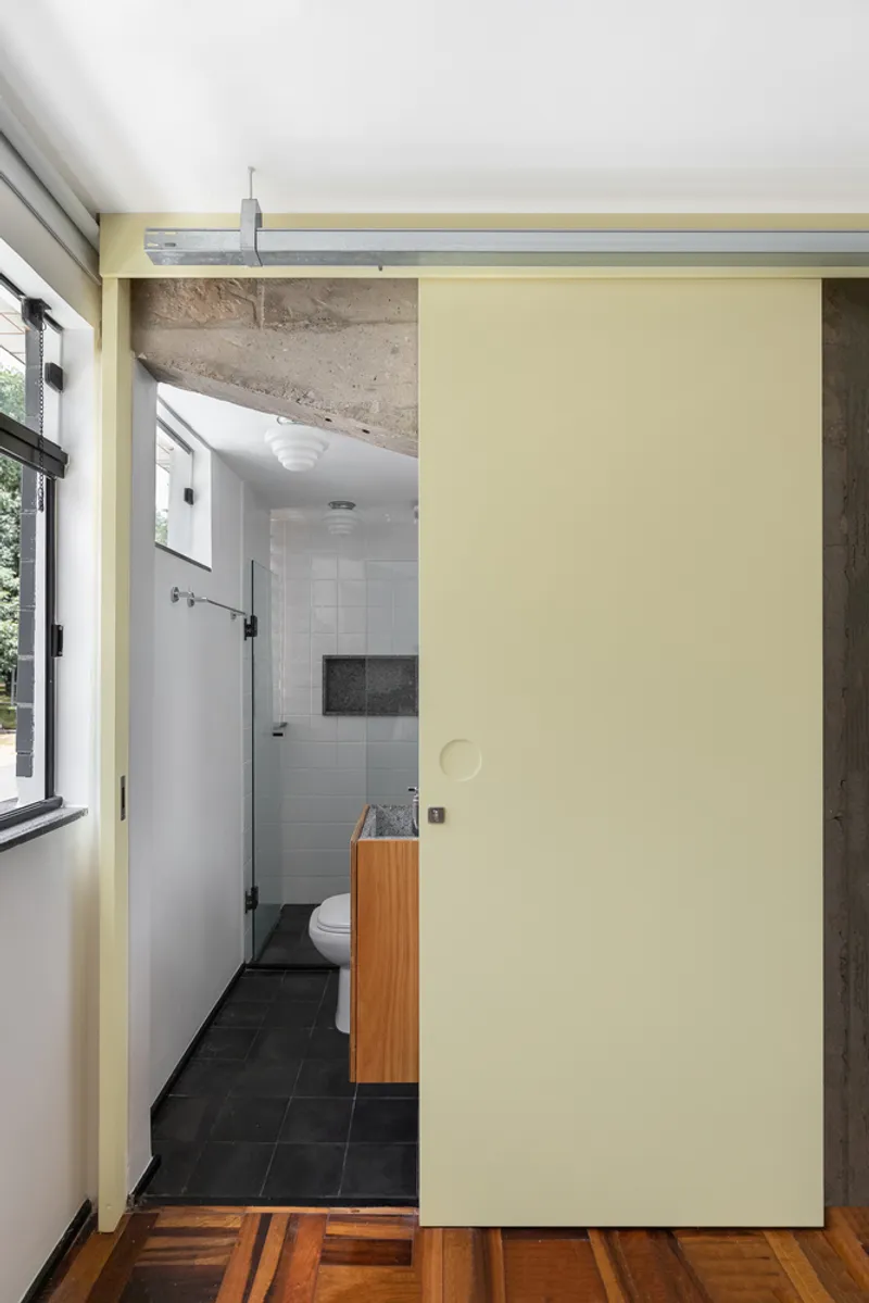 Pale yellow sliding door opening to bathroom with white tile and exposed concrete ceiling