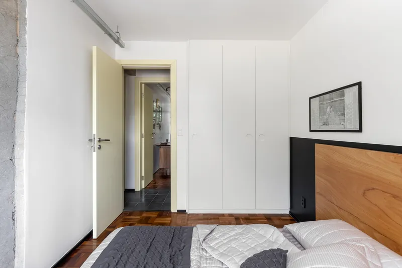 Bedroom with timber and black headboard, white built-in wardrobe and view through to dark-tiled corridor