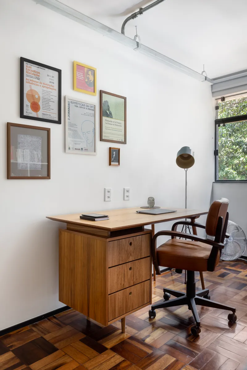 Home office with timber desk, parquet flooring and gallery wall of framed prints near window