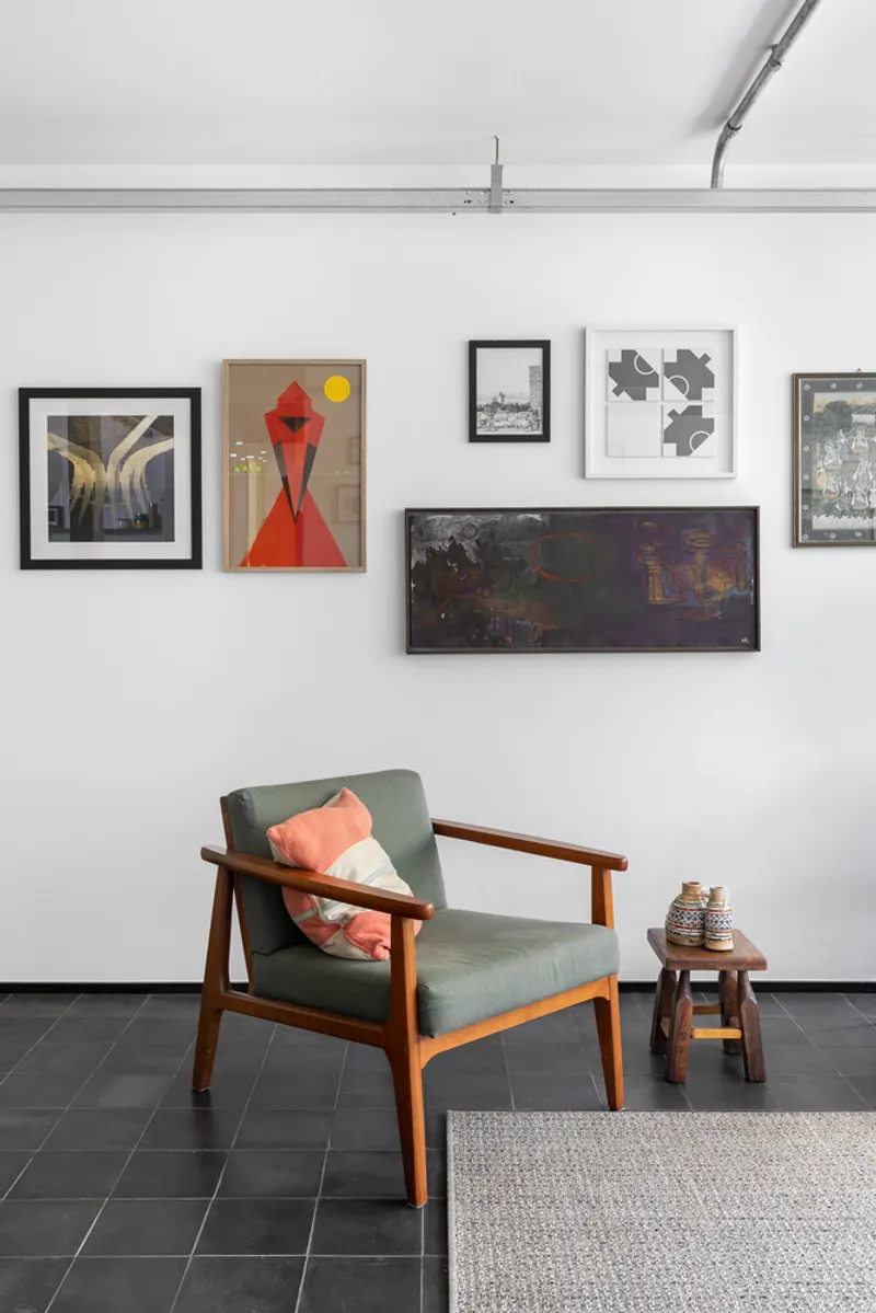 White wall with salon-hung artwork above timber armchair and dark tile floor