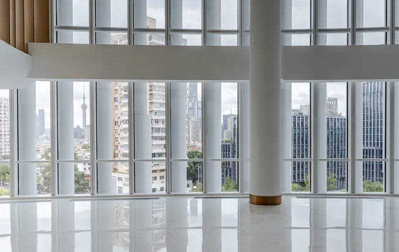 White column with timber base standing in a reflective floor beside tall gridded windows