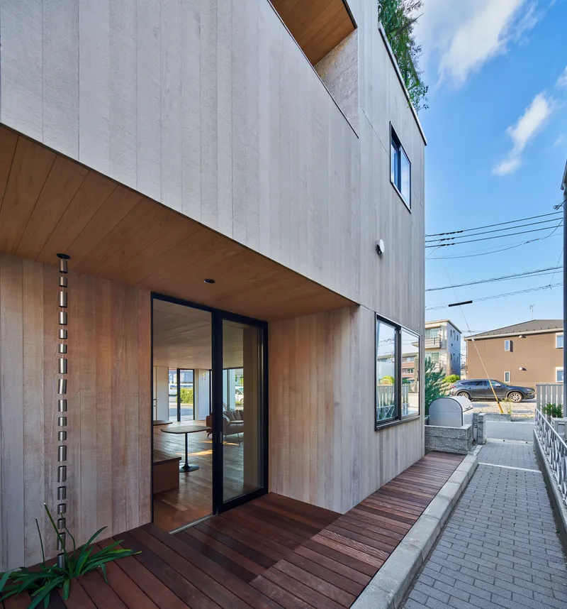 Timber entry deck with glass sliding doors set beneath cantilevered upper volume clad in pale wood panels