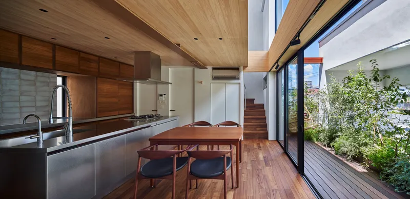Kitchen and dining area with stainless steel island opening onto timber deck through floor-to-ceiling glazing