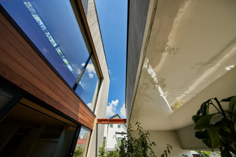 Narrow skylight between timber-clad volumes opening to bright blue sky with scattered clouds