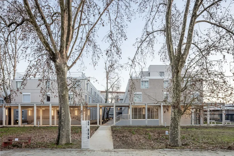 Front view of the raised housing complex with concrete columns and glazed ground floor framed by bare trees
