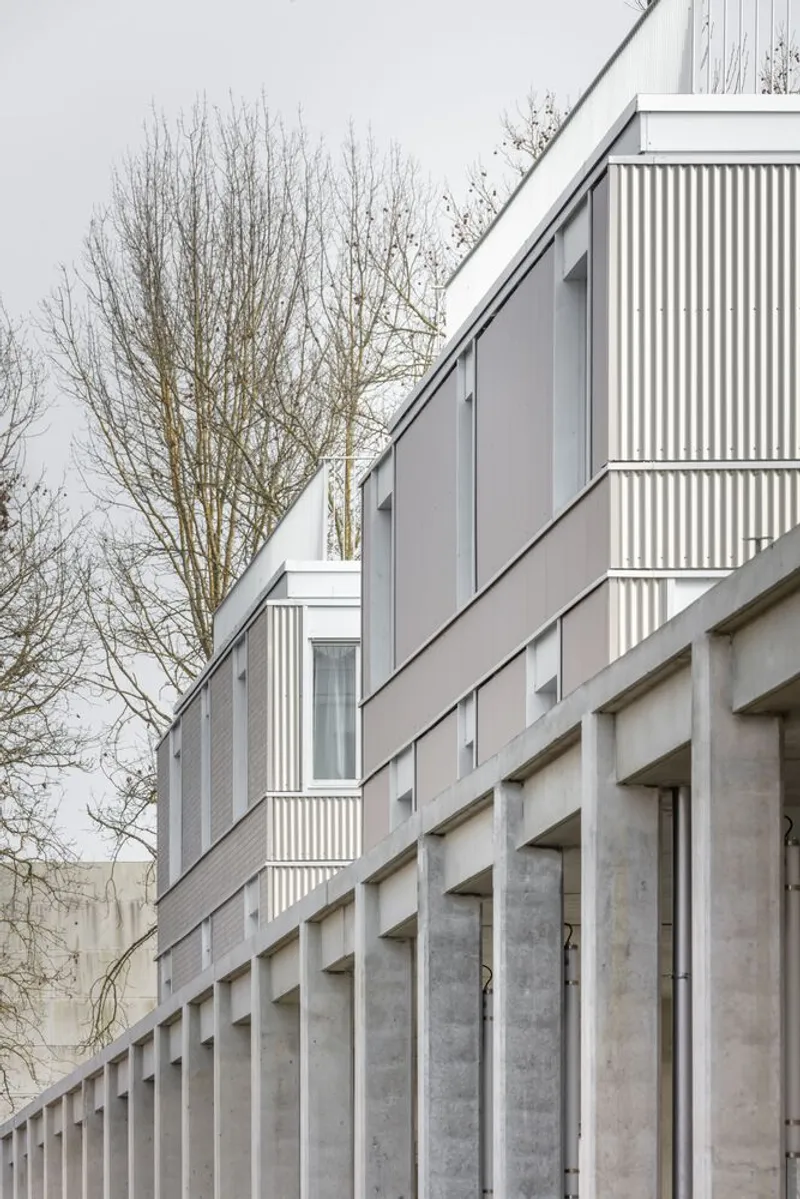 Upper facade of corrugated metal cladding with projecting balconies above a concrete colonnade base