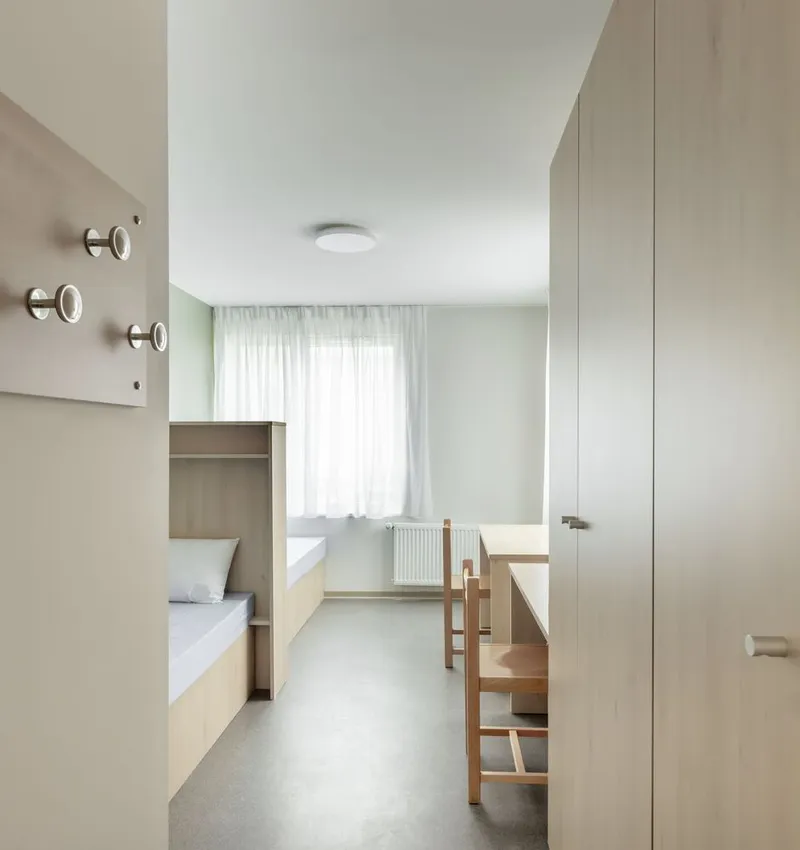 Compact sleeping room with bunk beds, built-in desk and wardrobe under soft daylight from sheer curtains