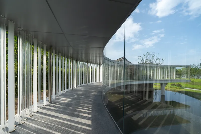 Interior corridor with vertical metal fins casting shadow patterns on curved glass wall and dark ceiling